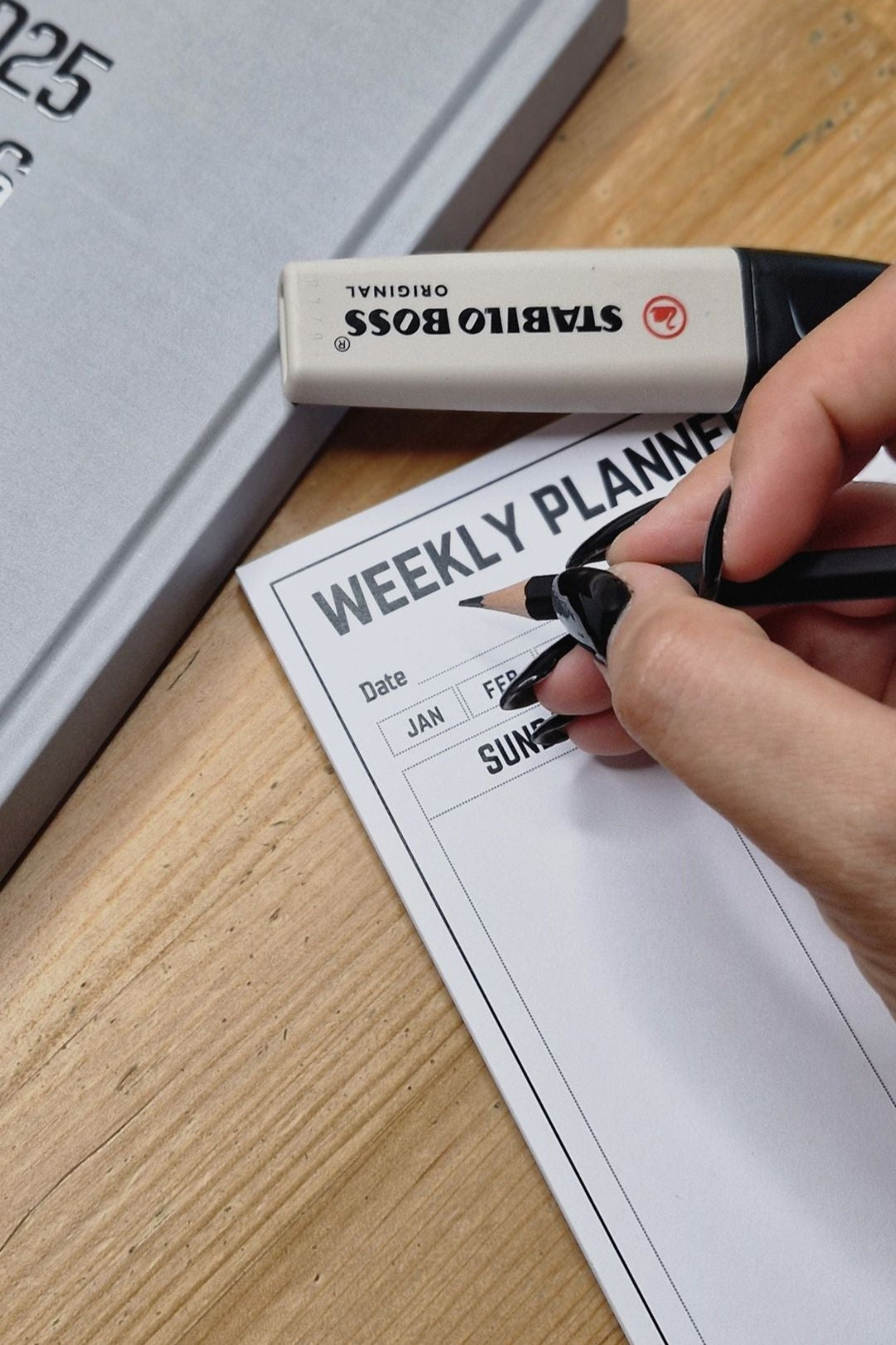 Person writing on a weekly planner with a Stabilo Boss pen, next to a Stabilo Boss box.